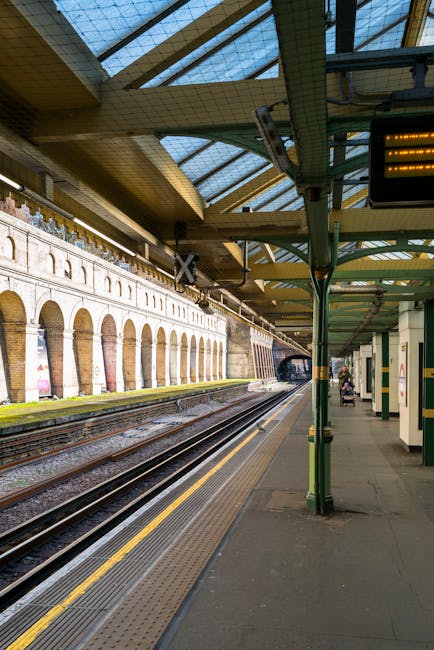 The image depicts an underground London Underground station platform at High Street Kensington, illuminated by warm artificial lighting. On the left side, a modern train with a white and grey exterior