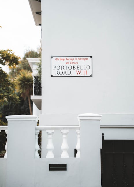 A white residential building with a small front garden enclosed by a low white wall featuring decorative balusters and a flat top, situated on Portobello Road in the Royal Borough of Kensington and Ch